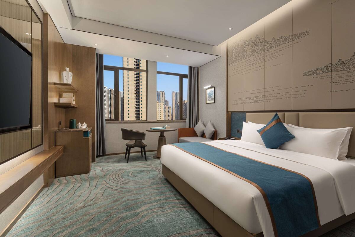 A hotel room with a large bed, a desk, a chair, and a TV.