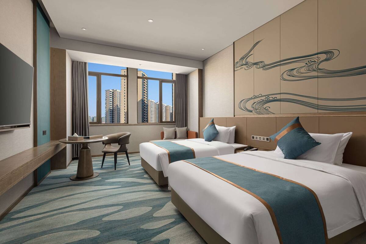 A hotel room with two beds, a desk, and a view of tall buildings.