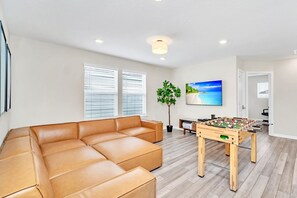 Una sala de estar moderna con un sofá de cuero, una mesa de fútbol y un televisor grande mostrando una playa.
