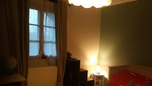A room with a window, a lamp, a radiator, a bed, and a small table.