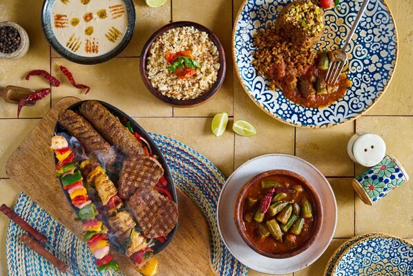 A variety of dishes including grilled meat, rice, and a bowl of stew, suggesting a diverse meal selection. - Benben By Dhara Hotels (Aswan)