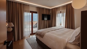 Ein modernes Hotelzimmer mit einem großen Bett, einem Flachbildfernseher und einem Balkon mit Vorhängen.