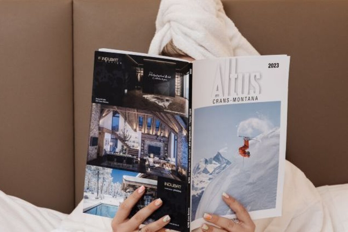 A person holding a magazine with a cover featuring a luxurious interior and a snowy mountain scene.