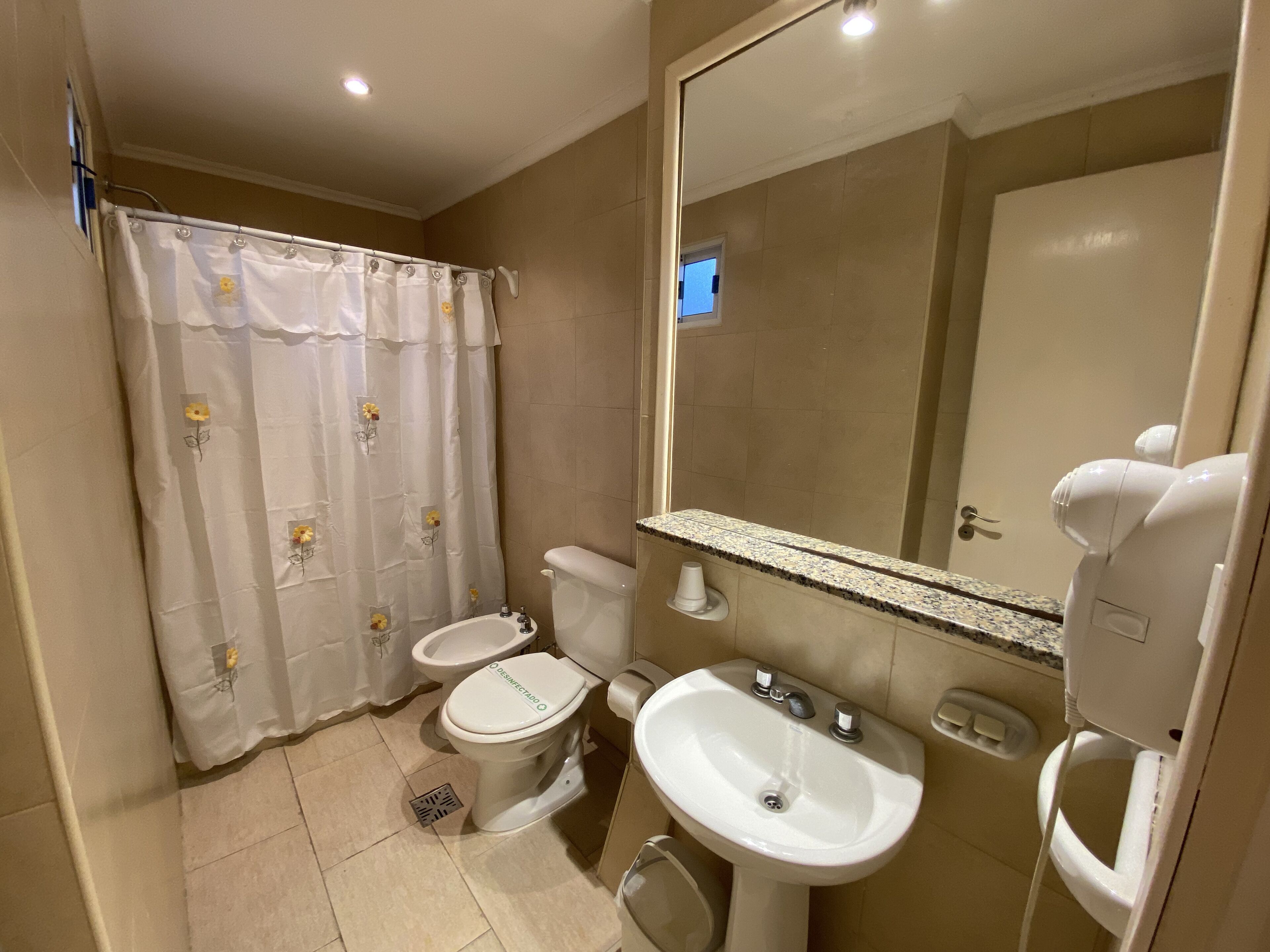 Un baño con inodoro, bidé, lavamanos y un espejo grande.