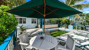 Un área junto a la piscina con una mesa y sillas, una sombrilla verde y una piscina pequeña.