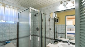Une salle de bain avec une douche à parois de verre, des toilettes, un lavabo avec un miroir et une fenêtre avec un rideau.