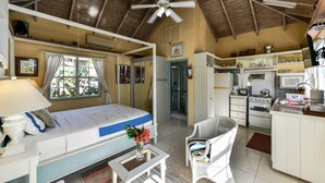 Une pièce de taille modeste comprenant un lit, une petite table avec un vase, une chaise, un coin cuisine et un ventilateur de plafond.