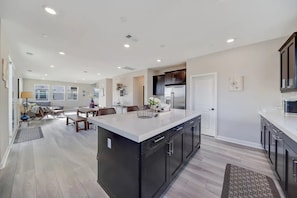 A modern kitchen with a large island, dark cabinetry, and a dining area with a sofa and table.