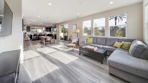 A spacious living area with a grey sofa, wooden coffee table, and a dining table with chairs. - Luxe Private Getaway in the Heart of Oceanside! (Oceanside)