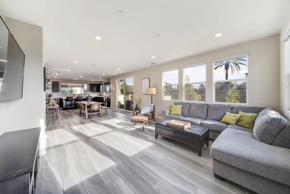 A spacious living area with a grey sofa, wooden coffee table, and a dining table with chairs.