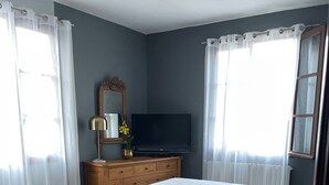 A bedroom with a bed, a dresser, a TV, and a window with curtains.