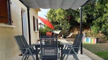 Un patio al aire libre con una mesa y sillas, un paraguas rojo y vistas a árboles y un edificio.
