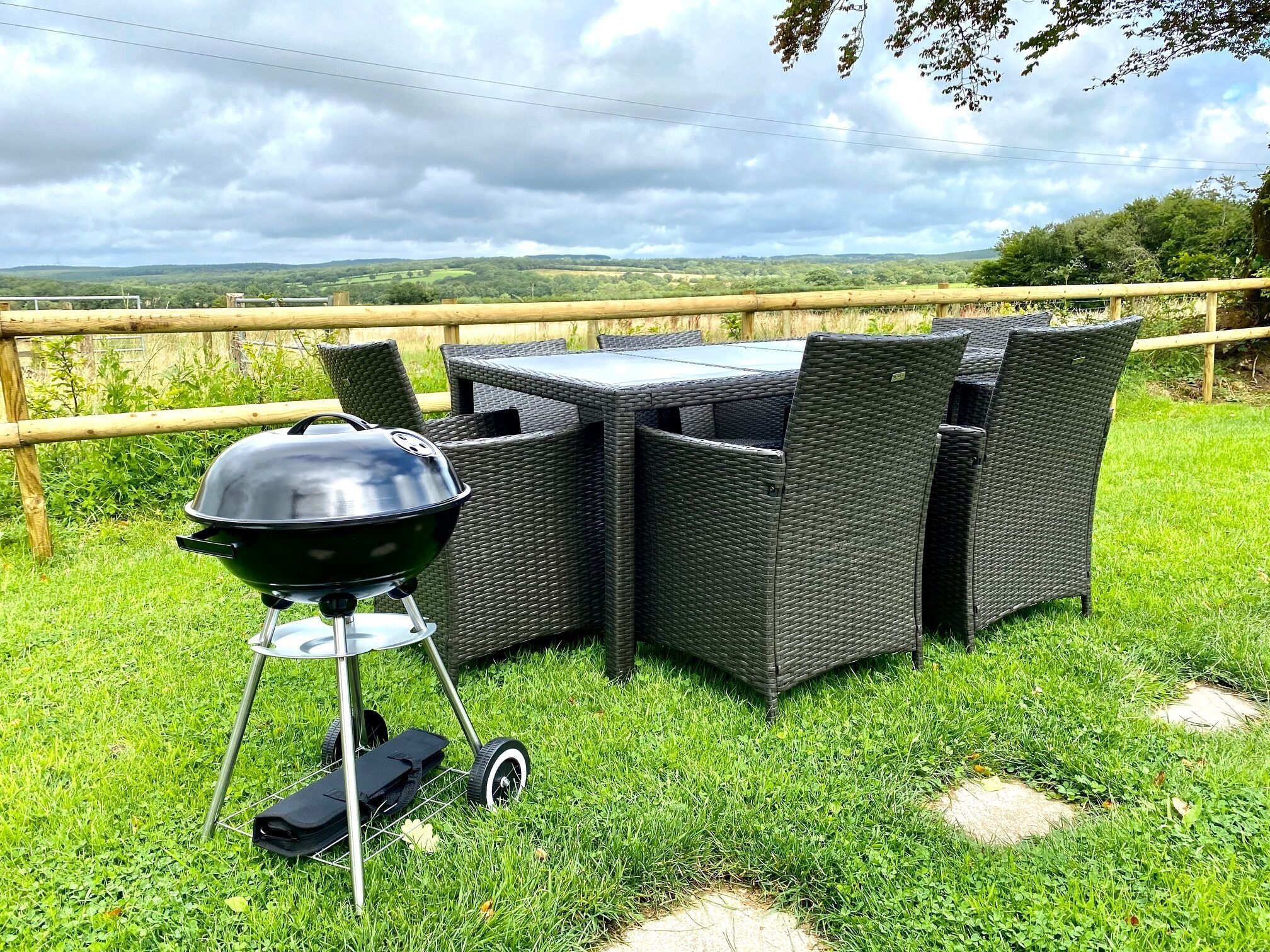 An outdoor dining area with a grill, wicker chairs, and a view of the countryside.