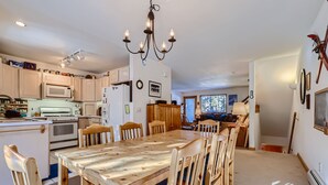 A spacious kitchen with a large wooden dining table and chairs, a chandelier, and a view into the living area. - Pinecreek #G- 3 BR: Close to Town- Shuttle to Slopes- Pool & Hot Tub Access (Breckenridge)