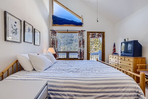 Une chambre à coucher avec un grand lit, une commode, un téléviseur et une fenêtre avec des rideaux.