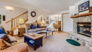 A cozy living room with a fireplace, a staircase, and a comfortable sofa. - Pinecreek #G- 3 BR: Close to Town- Shuttle to Slopes- Pool & Hot Tub Access (Breckenridge)
