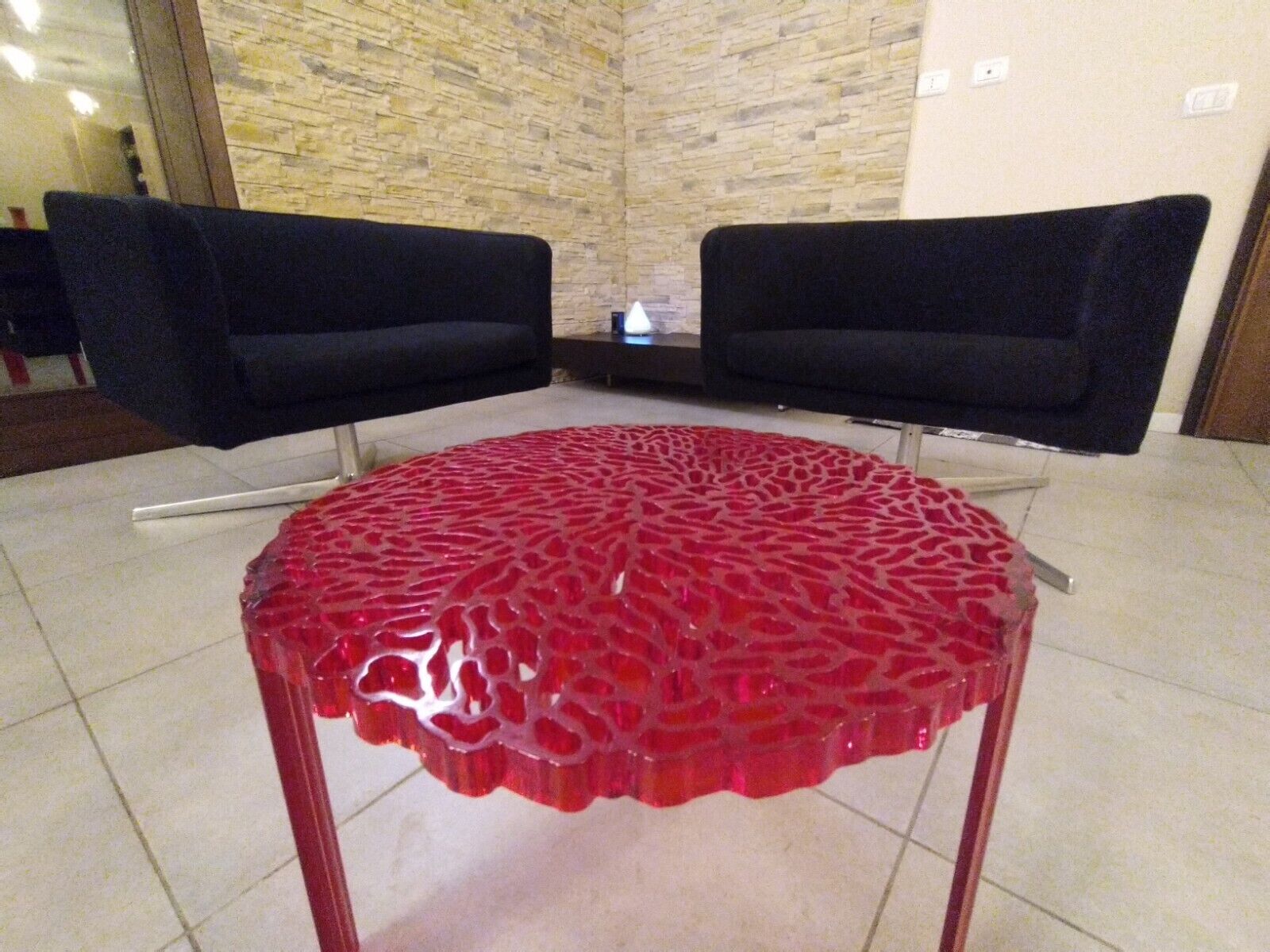 Una habitación con dos sillas negras, una mesa con estampado rojo y una pared de piedra.
