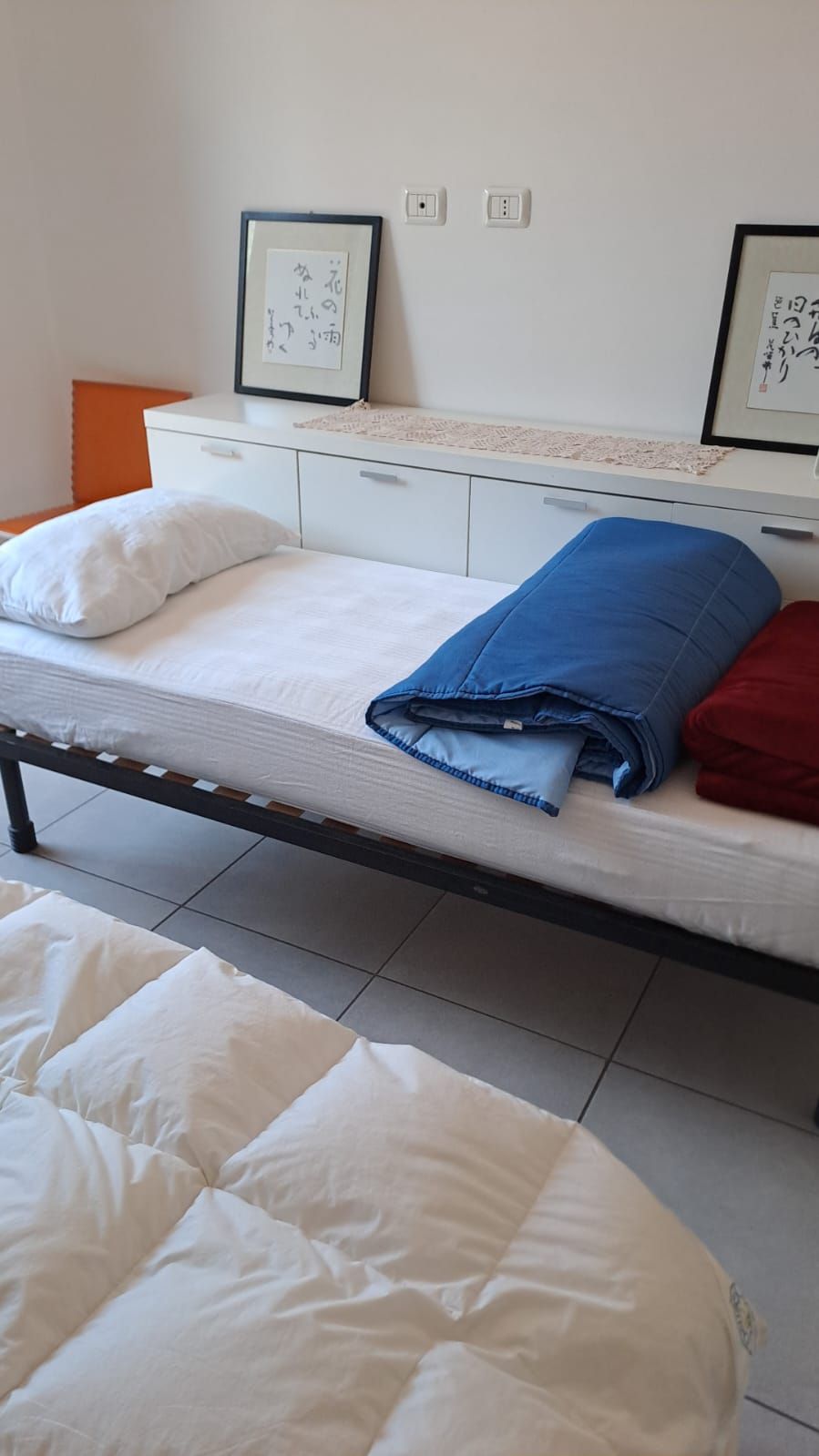 A bed with white and blue bedding, a white bedside table, and a white dresser with two framed pictures.