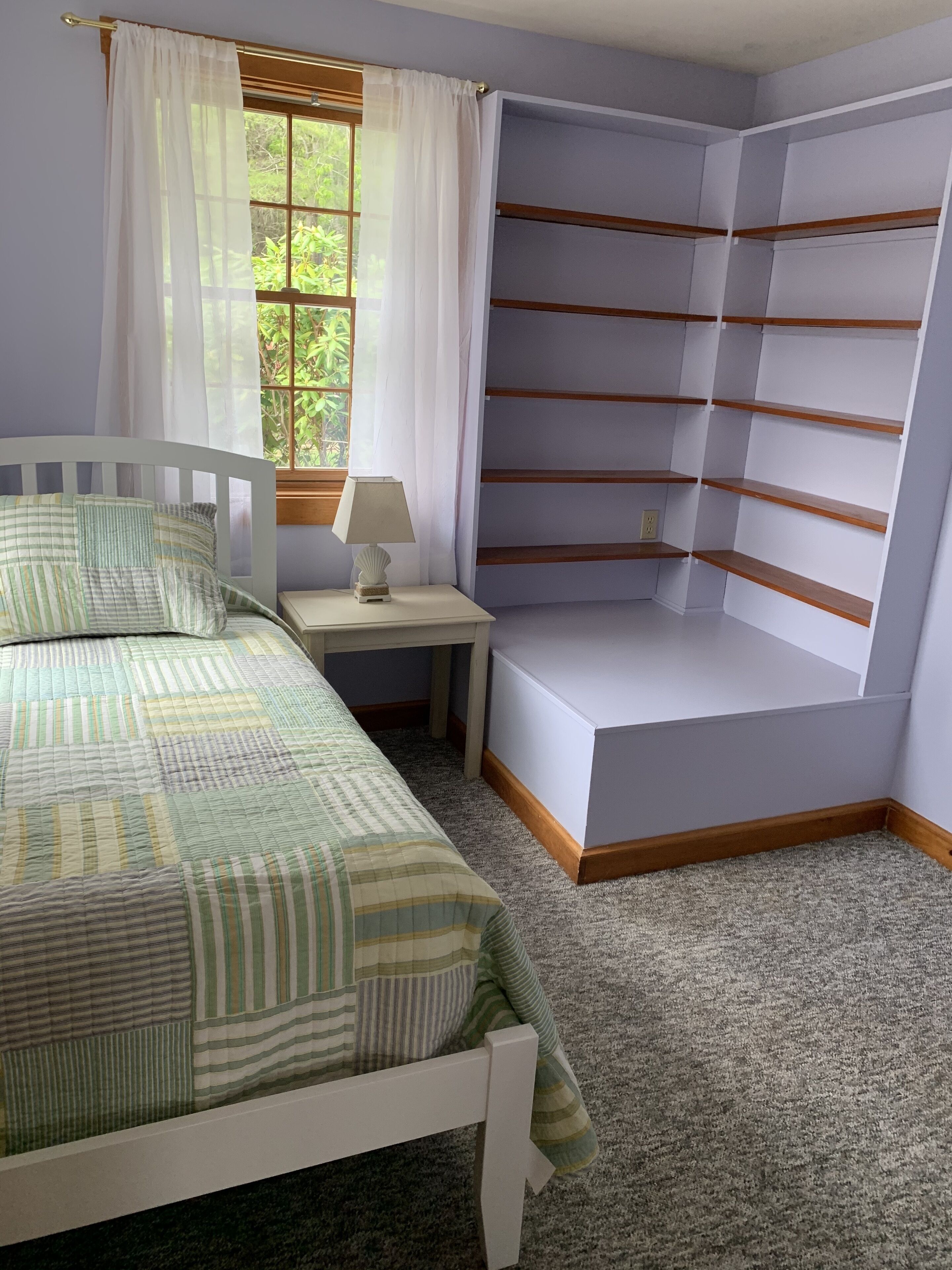 A bedroom with a bed, a nightstand, a lamp, and built-in shelving.
