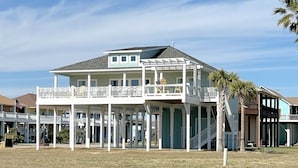 A two-story beachfront house with a balcony, a covered porch, and a staircase leading to the upper level.