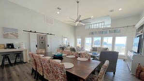 A spacious dining area with a large wooden table, patterned chairs, and a ceiling fan.