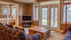 Ein Wohnzimmer mit einer Couch, einer Holzkiste, einem Fernseher und großen Schiebeglastüren zum Garten.