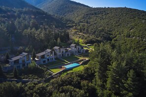 A modern resort with multiple buildings, a swimming pool, and lush surrounding forest.