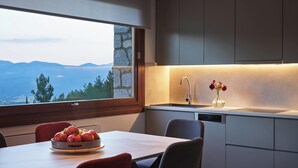 A modern kitchen with a large window, a bowl of fruit on the table, and a vase with flowers on the counter.