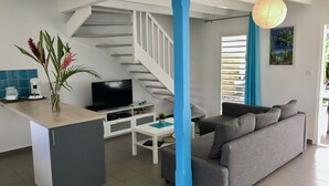 Ett modernt vardagsrum med en grå soffa, en platt-TV, en kaffemaskin och en trappa med en blå detalj.