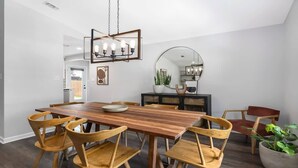 Un comedor con una mesa y sillas de madera, una araña, un espejo y una planta en maceta.