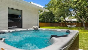 Un patio trasero con un jacuzzi, una terraza de madera y césped.