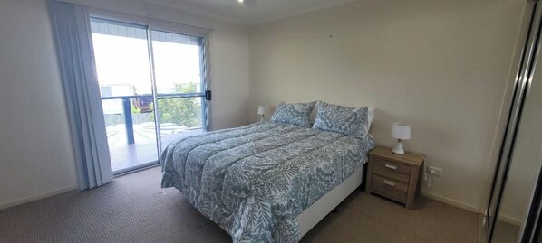 A bedroom with a bed, a nightstand, a lamp, and a sliding glass door leading to an outdoor area.