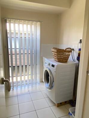 A laundry room with a washing machine, a basket on top, and a tiled floor.