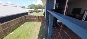 A residential backyard with a wooden fence, a grassy lawn, and a house with a blue exterior.