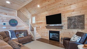 A cozy log cabin interior with a fireplace, a television mounted above it, and a staircase leading to an upper level. - Beautiful cottage with AMAZING view of Barren River Lake! (Scottsville)