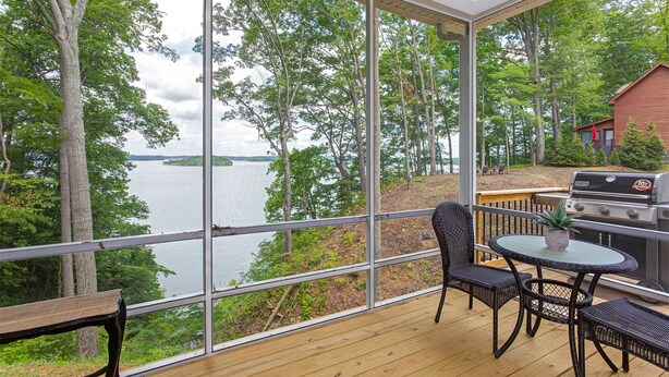 A covered deck with a view of a lake, a grill, and outdoor furniture. - Beautiful cottage with AMAZING view of Barren River Lake! (Scottsville)