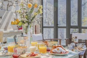 Ett frukostbord med olika sorters mat, en vas med blommor och en stenmur i bakgrunden.