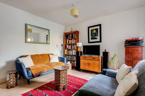 A living room with a blue sofa, a wooden bookshelf, a television, and a red patterned rug.