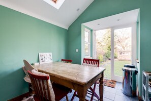 A dining area with a wooden table and chairs, a window, and a view of the garden.