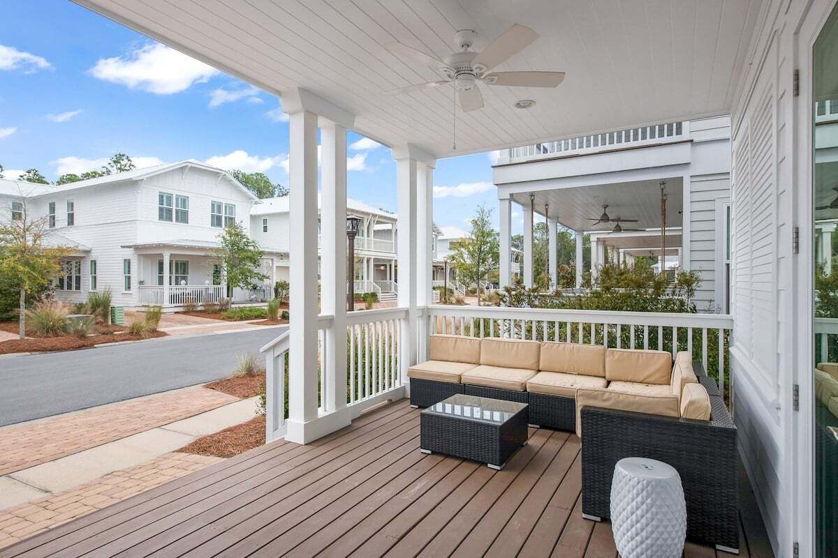 Une véranda avec un canapé et une table basse, des balustrades blanches et une vue sur les maisons voisines.