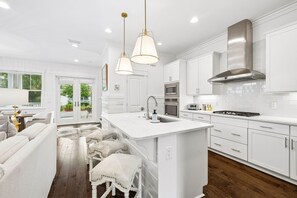 A modern kitchen with white cabinetry, a central island, stainless steel appliances, and pendant lighting.