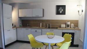 A modern kitchen with white cabinets, a round white table, and four yellow chairs.
