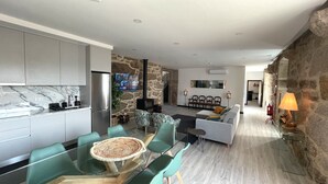 A modern kitchen with a marble countertop, a dining area with glass tables and chairs, a living room with a sofa and a TV, and a stone wall. - Tower House (Lapela)