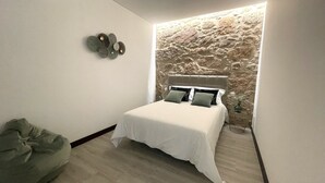 A modern bedroom with a stone accent wall, a bed with white bedding, and a green bean bag chair. - Tower House (Lapela)