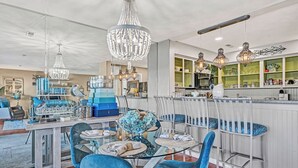A modern kitchen with a central island, pendant lights, and a dining area with blue chairs and a glass table.