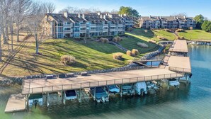 A lakeside residential complex with multiple apartment buildings, a dock with boats, and a well-maintained grassy area.