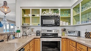 A modern kitchen with a built-in microwave, toaster, and oven, wooden cabinets, and a green 'Gather' sign on the wall.