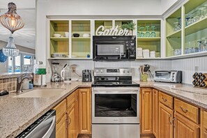 Une cuisine moderne équipée d’un four à micro-ondes, d’un grille-pain et d’un four encastrés, de placards en bois et d’un panneau vert portant l’inscription « Gather » au mur.
