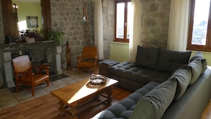 Uma sala de estar com parede de pedra, sofá de madeira, cadeira de madeira, mesa de madeira e um lustre.