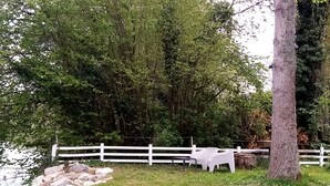 A white fence, a tree, and a grassy area with a body of water. - Waterfront Apartment in Garennes-sur-Eure at Le Havre de Paix - Sleeps 3–4  (Neuilly)